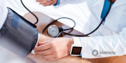 An image of a doctor's arm, wearing a fitness wearable, checking blood pressure of a patient.