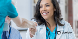 Female doctor shakes hands with a woman in nurse's uniform.